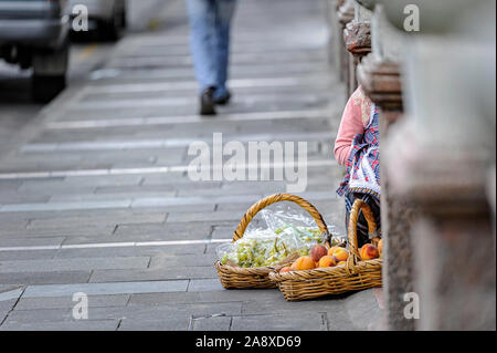 Zwei Körbe mit Äpfeln und Trauben, die auf einem Bürgersteig der Stadt platziert werden, während eine Person im Hintergrund läuft. Cuenca Ecuador Stockfoto