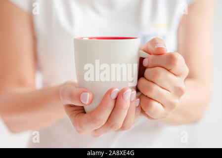 Frau in einem weißen T-Shirt hält Kaffee in eine weiße Schale Stockfoto