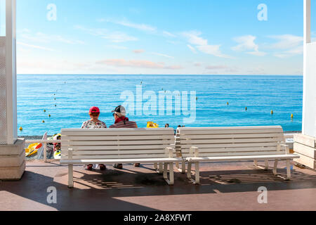 Ein älteres Paar auf einer Bank an der Promenade des Anglais und genießen Sie Blick auf den Strand und die Bucht der Engel auf dem Mittelmeer Cote d'Azur. Stockfoto