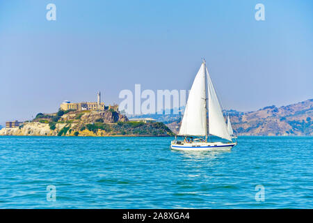 Blick auf Alcatraz Island mit einem segelboot, das an der San Francisco Bay in San Francisco vorbeiführt. Stockfoto
