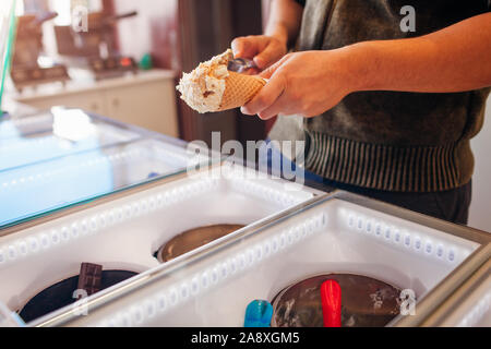 Verkäufer Füllung Waffel Kegel mit Eis. Vanille Aroma mit Cookies Krümel Stockfoto