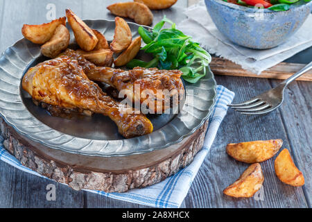 Chicken Drumsticks in Ingwer Bier Sauce mit Kartoffelecken und Salat auf einen Teller Stockfoto