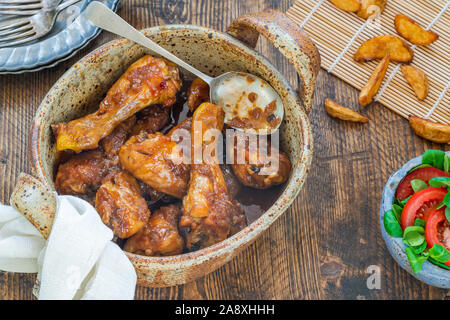 Chicken Drumsticks in Ingwer Bier Sauce mit Kartoffelecken und Salat auf rustikalen Holztisch Stockfoto