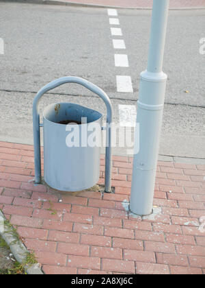 Metall Urne in der Nähe der Straße. Ein Metall Mülleimer steht in der Nähe der A-Säule auf dem Bürgersteig. Schmieden von Mülltonnen steht in der Nähe eine Bank, auf dem Bürgersteig Stockfoto