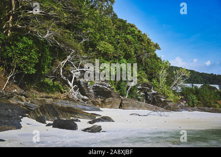 Hanglage mit schwarzen Felsen und grünen Bäumen, Pflanzen am Ufer des wunderschönen exotischen Sandstrand und eine atemberaubende Cenang Beach in Insel Langkawi, in Malaysi Stockfoto