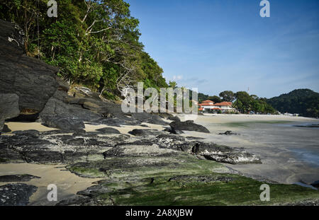 Hanglage mit schwarzen Felsen und grünen Bäumen, Pflanzen am Ufer des wunderschönen exotischen Sandstrand und eine atemberaubende Cenang Beach in Insel Langkawi, in Malaysi Stockfoto