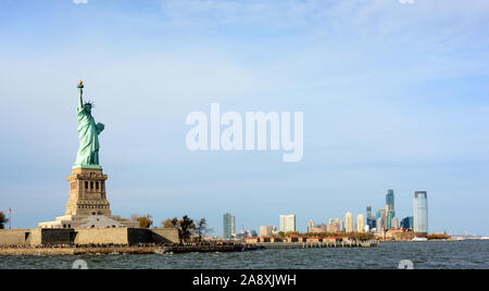 Die Freiheitsstatue und Ellis Island mit der Jersey City Skyline im Hintergrund. Stockfoto