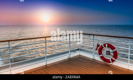 Landschaftlich schöne Aussicht auf den Sonnenuntergang vom Deck eines Kreuzfahrtschiffes mit Sicherheitsgeländer im Vordergrund. Stockfoto