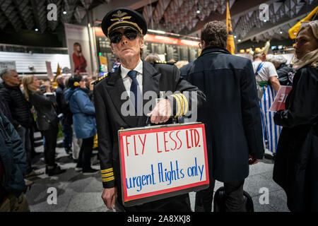 11 November 2019, Hessen, Frankfurt/Main: ein Demonstrant verkleidet als Pilot hält einen Koffer mit der Inschrift "Weniger fliegen - Dringend Flüge nur' an der 300 Montag Demonstration der Anti - Fluglärm Kämpfer im Terminal 1 des Frankfurter Flughafens. Foto: Frank Rumpenhorst/dpa Stockfoto