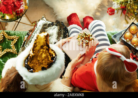 Obere Ansicht von Mutter versuchen, ein Buch als Weihnachtsgeschenk zu unglücklichen Tochter beim Sitzen auf der Couch im Wohnzimmer zu Weihnachten zu geben. Stockfoto