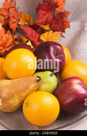 Herbst frisches Obst Herzstück in einer transparenten Schüssel und bunten Ahornblätter im Hintergrund. Ein sackleinen Stück Stoff, das ist der Hintergrund. Stockfoto