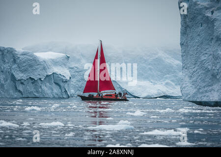 Ein kleines Schiff zwischen Eisbergen. Segelboot Kreuzfahrt unter schwimmende Eisberge in der Diskobucht Gletscher Mitternachtssonne Ilulissat, Grönland. Studium der Ph Stockfoto