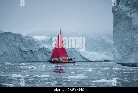 Ein kleines Schiff zwischen Eisbergen. Segelboot Kreuzfahrt unter schwimmende Eisberge in der Diskobucht Gletscher Mitternachtssonne Ilulissat, Grönland. Studium der Ph Stockfoto