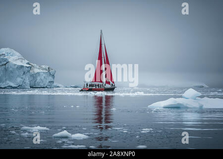 Ein kleines Schiff zwischen Eisbergen. Segelboot Kreuzfahrt unter schwimmende Eisberge in der Diskobucht Gletscher Mitternachtssonne Ilulissat, Grönland. Studium der Ph Stockfoto