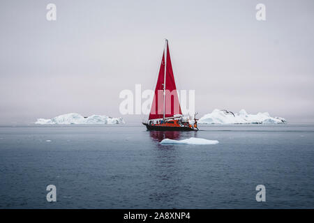 Ein kleines Schiff zwischen Eisbergen. Segelboot Kreuzfahrt unter schwimmende Eisberge in der Diskobucht Gletscher Mitternachtssonne Ilulissat, Grönland. Studium der Ph Stockfoto