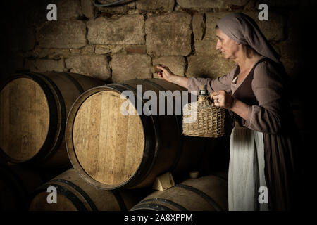 Die Frau in der mittelalterlichen bäuerlichen Outfit prüfen Wein Fässer im Keller einer Eigenschaft freigegeben Authentische mittelalterliche Schloss in Frankreich Stockfoto