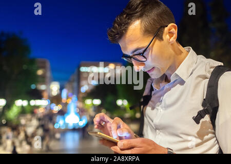 Mann mit Smartphone auf Stadt Straße in Athen, Griechenland in der Nacht. Kerl schreiben Nachricht in Park Stockfoto