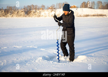 Ein Fischer Bohrer ein Loch im Eis, um Fische zu fangen, Tom River in Kemerovo, Russland Stockfoto