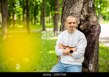 Mann lehnte sich auf Baum in Hellgrau Sweatshirt bekleidet Stockfoto