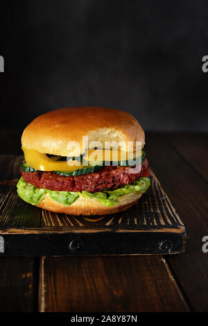 Gebissen vegetarische Burger auf Holzbrett auf dunklem Hintergrund Stockfoto