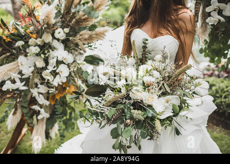 Woman Holding in den Händen große Hochzeit Blumenstrauß in Boho Style. Getrocknete Blumen, weiße Rosen und Orchideen, Vogelfedern im Dekor. Floristische Konzept. Stockfoto