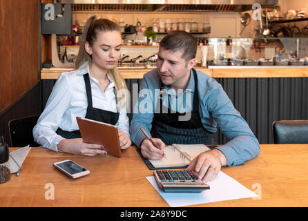 Neue Besitzer kleiner Unternehmen zählen die Einnahmen und Ausgaben - Start-up-Unternehmer, Frau und Mann, Geschäftsleute, Buchhaltung mit Taschenrechner und Tabl Stockfoto