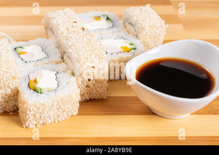 Sushi, Brötchen in Weiß Sesam, mit Käse, Avocado und Garnelen. Auf der Planke. Auf einem roten Hintergrund. Stockfoto