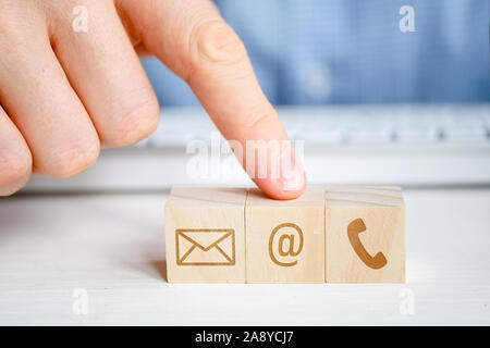 Ein Mann zeigt auf einen Holzwürfel mit dem Bild eines e-Symbol neben einer Telefon- und ein Schreiben mit der Hand. Kontakt Konzept für die Kommunikation. Clo Stockfoto