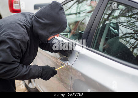 Ein Räuber in Schwarz holding Brecheisens ein Fahrer in einem Auto gekleidet. Auto Dieb, Autodiebstahl Konzept. Stockfoto