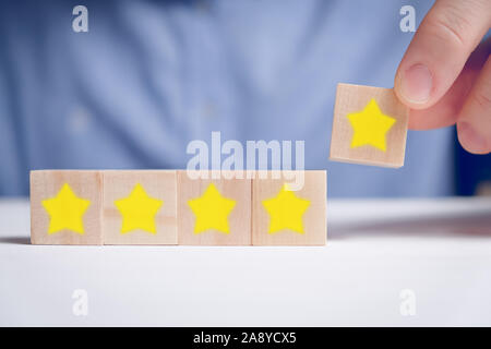 Ein Mann in einem Hemd abstrakt Bewertung fünf Sterne auf Holz Würfel. Beste Punktzahl. Close Up. Stockfoto