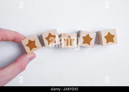 Ein Mann legt fünf Sterne auf Holzwürfel mit seiner Hand, die die beste Bewertung. Beste Punktzahl. Flach. Close Up. Stockfoto