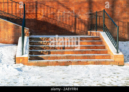 Fragment eines schneebedeckten Treppe mit geschmiedetem Geländer vor dem Hintergrund einer Backsteingebäude close-up. Winter urbanen Landschaft. Stockfoto