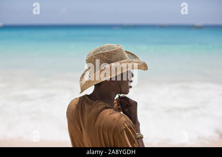 Junger Mann mit einem Stroh Sonnenhut beim Stehen auf einem Strand mit Meerblick. Stockfoto