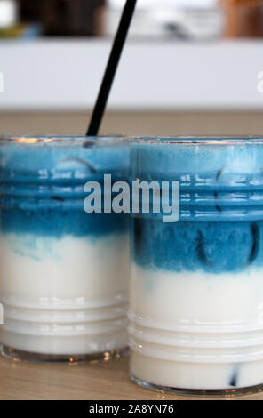 Zwei Gläser iced Erbse latte. Blue Tee 2-in-1-Cocktail mit Milch auf Holztisch mit schwarz Stroh und Eis. Nicht alkoholische und alkoholfreie Gesund kalt trinken. Stockfoto