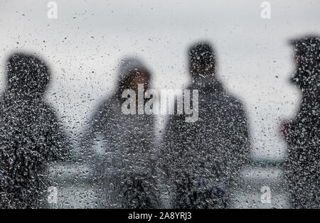 Menschen, die auf der Außenseite Deck auf einem Washington State Ferry im Regen durch ein Fenster mit Regentropfen fallen gesehen, den Schwerpunkt auf die Regentropfen. Stockfoto