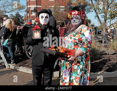 Ein paar in bunten skull Make up und Maske feiern Dia de los Muertos in Cleveland, Ohio, USA halten momentos von Lieben, die weitergegeben. Stockfoto