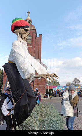 Ein überlebensgroßes Skelett ragt über einer Mutter mit ihrem Baby während der 2019 Day of the Dead-Fest in Cleveland, Ohio, USA. Stockfoto