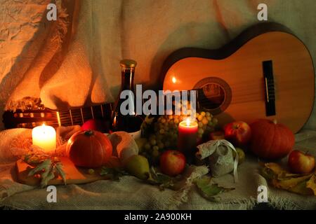 Wein und Gitarre. Äpfel, Trauben und Birnen mit Kürbissen und Blätter mit Kerzen Flamme stehen auf Tabelle mit Sack Stockfoto