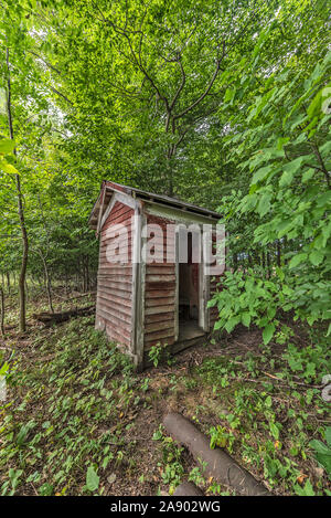 Plumpsklo im Wald hat sich von einem hellen Rot und eine verwitterte Rot verblasst, als es über eine Reihe von Jahren nicht verwendeten sitzt Stockfoto