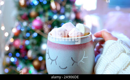 Frau mit heißer Schokolade vor im Trend rosa und Rose Gold Getrimmt Weihnachtsbaum. Stockfoto