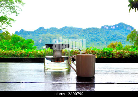 Ein teeei auf einer Holzbank mit Kräutertee auf einer Holzbank mit Bergen im Hintergrund Stockfoto