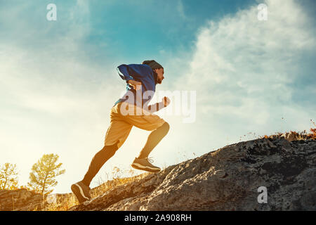 Skyrunner Athlet läuft bergauf gegen Sonnenuntergang bzw. Sonnenaufgang Himmel und Sonne. Skyrunning Konzept Stockfoto