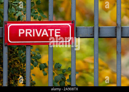 Rote metall Schild mit der Aufschrift-PRIVATE auf einem dekorativen Metallzaun, defokussierten Bäume im Herbst in background-image Stockfoto