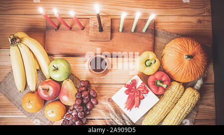 Kwanzaa urlaub Konzept mit sieben Kerzen Rot, Schwarz und Grün schmücken, Geschenkbox, Kürbis, Mais und Obst auf hölzernen Schreibtisch und Hintergrund. Stockfoto