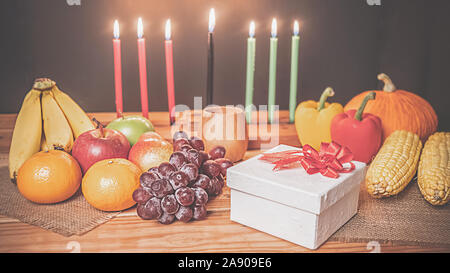 Kwanzaa urlaub Konzept mit sieben Kerzen Rot, Schwarz und Grün schmücken, Geschenkbox, Kürbis, Mais und Obst auf hölzernen Schreibtisch und Hintergrund. Stockfoto