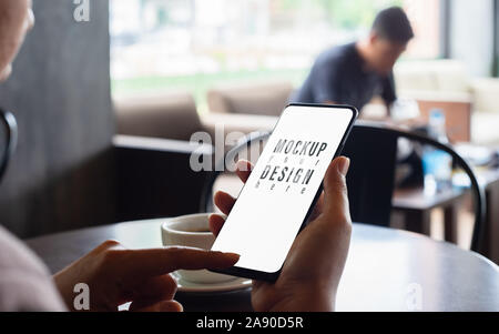 Mockup Bild von Hand und mit Hilfe von mobilen Smart Phone mit leeren weißen Bildschirm in einem Coffee Shop Stockfoto