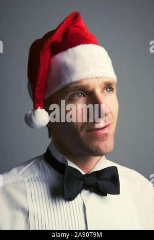 Portrait des jungen Mannes in formalen Smoking Smoking und Santa hat sich mit einem nachdenklichen Ausdruck Stockfoto