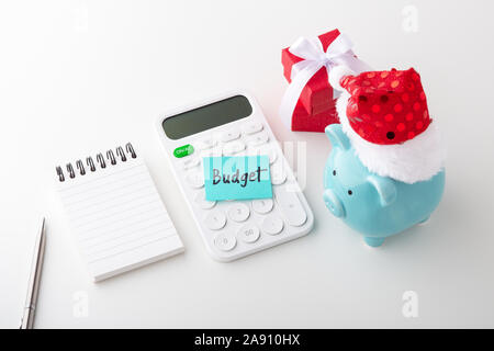 Piggy Bank tragen Mütze mit Word Budgets für Taschenrechner und Notizblock mit Stift, Weihnachten retten und Budget Konzept Stockfoto