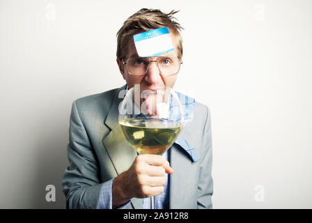 Betrunken im Büro mit einem Namensschild auf seine Stirn lecken ein übergroßes Glas Wein stecken Stockfoto