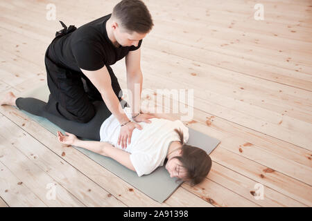 Der Mensch tut Rückenmassage von liegende Frau auf grauem Teppich in der Turnhalle Stockfoto